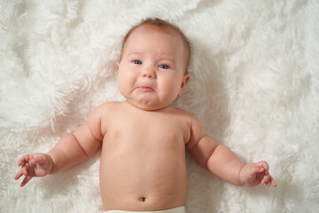 portrait of a crying baby lying on his back on a white comforter