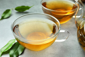Fresh green tea in glass cups and leaves on grey table, closeup