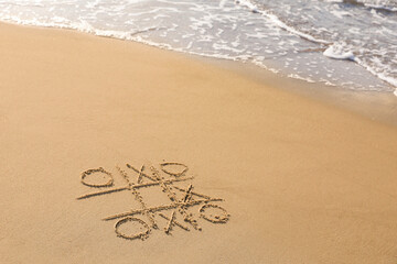 Tic tac toe game drawn on sand near sea, space for text