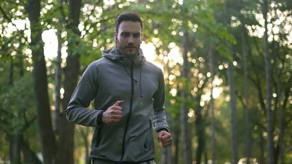 Young handsome athlete with earbuds running in the forest. 