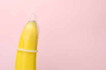 Banana with condom on pink background, closeup and space for text. Safe sex concept