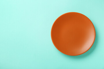 Clean orange plate on turquoise background, top view. Space for text