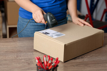 Post office worker with scanner reading parcel barcode at counter, closeup
