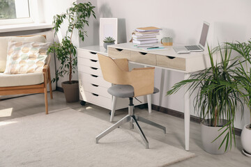 Beautiful workplace with laptop on white wooden table, chair and houseplants in room