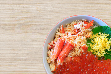 Bowl of rice topped with red king crab meat and Salmon roe on wood background, close up.