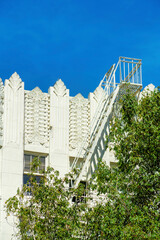 Decorative apartment building with hidden fire saftey escape ladder with front yard foliage and trees on white building midday sun