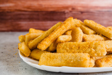 Fish sticks in a crunchy golden breading close-up on white plate on the kitchen table