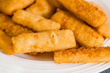 Fish sticks in a crunchy golden breading close-up on white plate on the kitchen table
