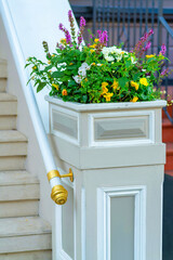 Front porch plant on gaurd banister with metal hand rail and decorative white and gray paint and accents with stairs