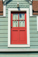 Red hidden door on side of building with white trim on the frame and green gray exterior horizontally slatted wood or timber house