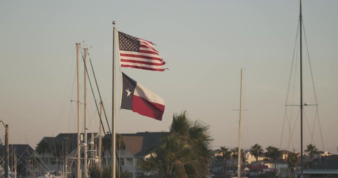 A frayed American flag flies over an intact Texas flag at a marina near Aransas Pass, Texas.