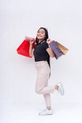 A young working woman in a dark top and khaki pants holding shopping bags on both hands after going on a shopping spree. Isolated on a white background. Retail and sale concepts.