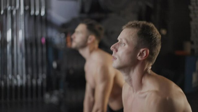 Two young shirtless men finishing with swinging heavy kettlebell in a gym. Healthy lifestyle concept. Slow motion. 