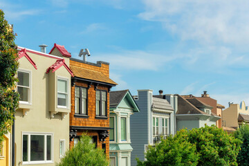 Row of colorful houses with brown beige and gray with sunny front yard trees and blue sky background