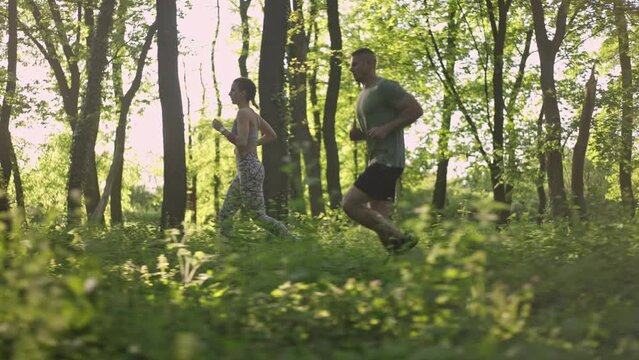 Side view of two young people running in the sunny forest. Slow motion. Healthy lifestyle concept.