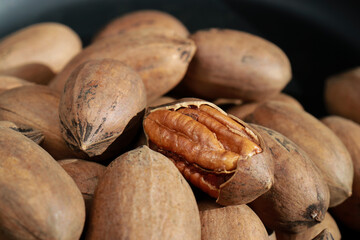 close up of pecan nuts in shell, one nut cracked, background 