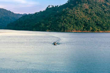 VIew of long-tailed boat floating on blue river in mountain with green forest. River in Khun Dan Prakan Chon Dam in Thailand. Landscape. Tourists on a boat to enjoy scenery in evening. Tourism concept