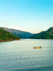 Fototapeta na wymiar VIew of long-tailed boat floating on blue river in mountain with green forest. River in Khun Dan Prakan Chon Dam in Thailand. Landscape. Tourists on a boat to enjoy scenery in evening. Tourism concept