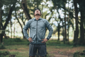 Naklejka na ściany i meble A man wearing earphones and stretching before running. Young man workout before fitness training in the forest. Healthy and exercise warming up.