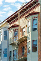 Brick building facade with white paint on exterior with brown metal fire escape ladder and flate roof