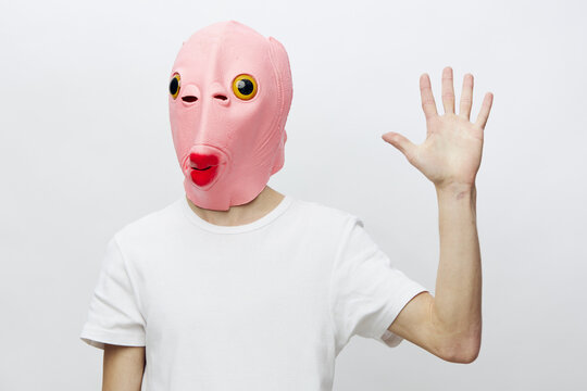 a man in a pink mask in the form of a fish on a light background shows five fingers