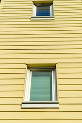 Horizontally slatted wood house facade with white accent paint around two hidden windows on the exterior of building