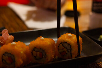 Chopsticks taking sushi roll with orange tobiko. Traditional Japanese food, low key concepts