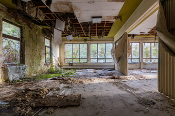 Abandoned psychiatric ward, a large room with broken ceiling, moss growing on the floor.