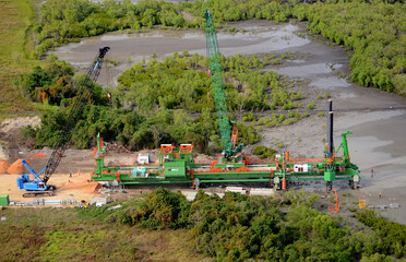 PNG-constructing a road across swamp lands using special machinery. This machinery stamps pylons into the more solid underwater terrain for a stable base.