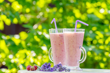 Glass of fresh strawberry milkshake, smoothie and fresh strawberries in garden on wooden table and green background. Healthy food and drink concept.