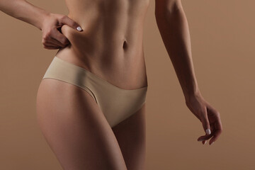 Thin young woman in underwear on beige background