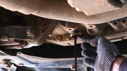 The hands of an auto mechanic unscrew the screw to drain the old engine oil under car. Replacing and draining old engine oil from the car. Car service and car care concept.
