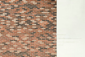 A brick wall with one third plastered over and painted white. Red, orange and brown bricks seen on an exposed brick wall. Weathered wall with surface wear, marks and cracks