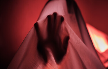 Hand, fabric and red with a person under a sheet in a bedroom or studio on a red background for...