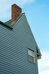 Slatted wooden house facade with red brick chimney and black accent paint near roof in late afternoon shade with blue sky background