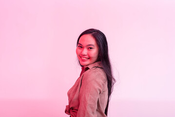 A happy and lively young asian woman posing behind a plain background with hot pink neon effect.