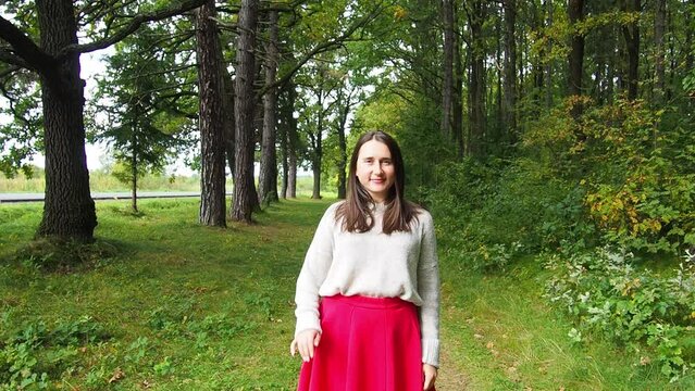 Young girl corrects long dark hair. Beautiful woman in gray sweater and red skirt posing in the forest on a sunny autumn day. Walking and relaxing in the woods.