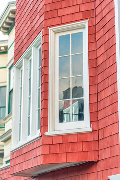 Bay window on cubby in side of red slatted wood building with white accent paint around glass windows in the neighborhood