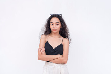 A slim and confident Filipino woman with long curly hair in her early 20s. Wearing a black spaghetti strap blouse and white pants. Arms crossed. Isolated on a white background.