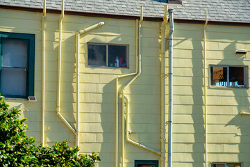 Yellow house facade with electric and water pipes on side of building with wooden timber slats and...