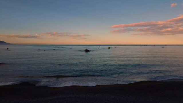 Rising drone shot out to sea at dusk with rocks in the water. Ocean and sea stock videos.