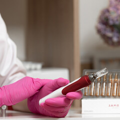 The beautician holds in his hands a dermapen, a tool for mesotherapy and cell regeneration.