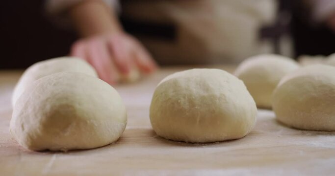 The baker rolls out the dough for buns on the board. Working in a bakery
