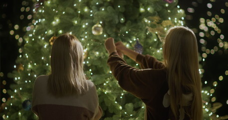 Mom and daughter decorate the Christmas tree together. Christmas eve and cozy house