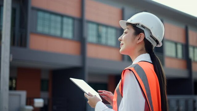 Serious engineer woman Using tablet for checking and maintenance to inspection at modern home building construction. Architect female looking forward with white safety helmet in construction site.