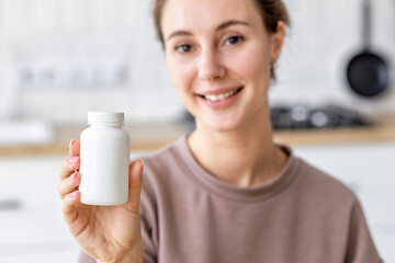 Happy young caucasian woman holding bottle of dietary supplements or vitamins in her hands. Close...