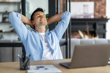 Satisfied young male businessman resting at workplace in the office, put his hands behind his head....