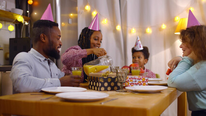 Happy family celebrating birthday of cute preteen boy clinking glasses with orange juice