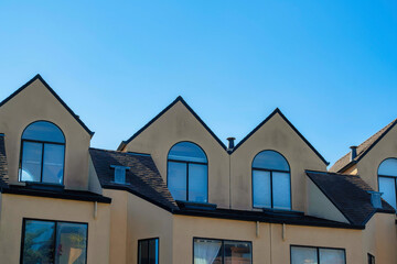 Row of beige stucco houses in the neighborhood with homes in the shade with round glass windows and blue sky background