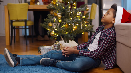 Portrait of sad African-American child sitting on floor alone during christmas celebration